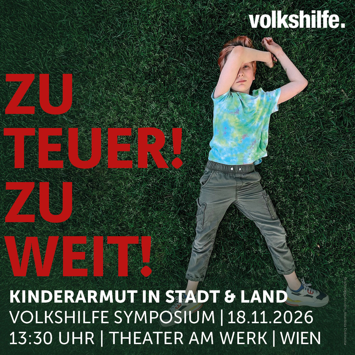 Logo und Schriftzug Save the Date: Zu teuer! Zu Weit! Kinderarmut in Stadt &amp; Land - Volkshilfe Symposium 2026, 18.11.2026, 13:30, Theater am Werk, Wien, hinter der Schrift ist ein Foto von einem Kind zu sehen. Das Kind liegt in der Wiese, den linken Arm über dem Kopf, der rechte Arm liegt neben dem Kopf in der Wiese. Das Kind Blickt in die Kamera.